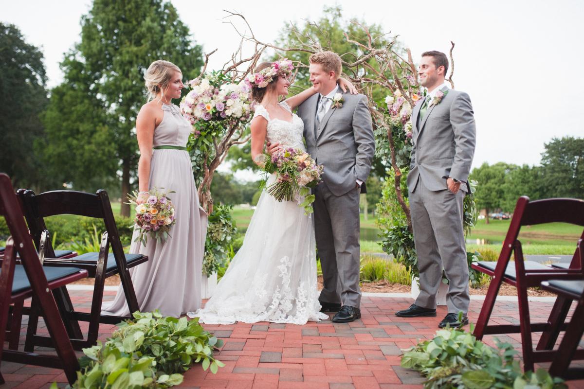 Bride, Groom, and Two Members of Wedding Party in Front of Wooded Archway