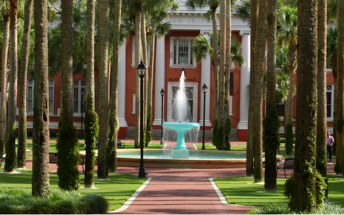 A row of trees and water fountain in front of a large hall building.